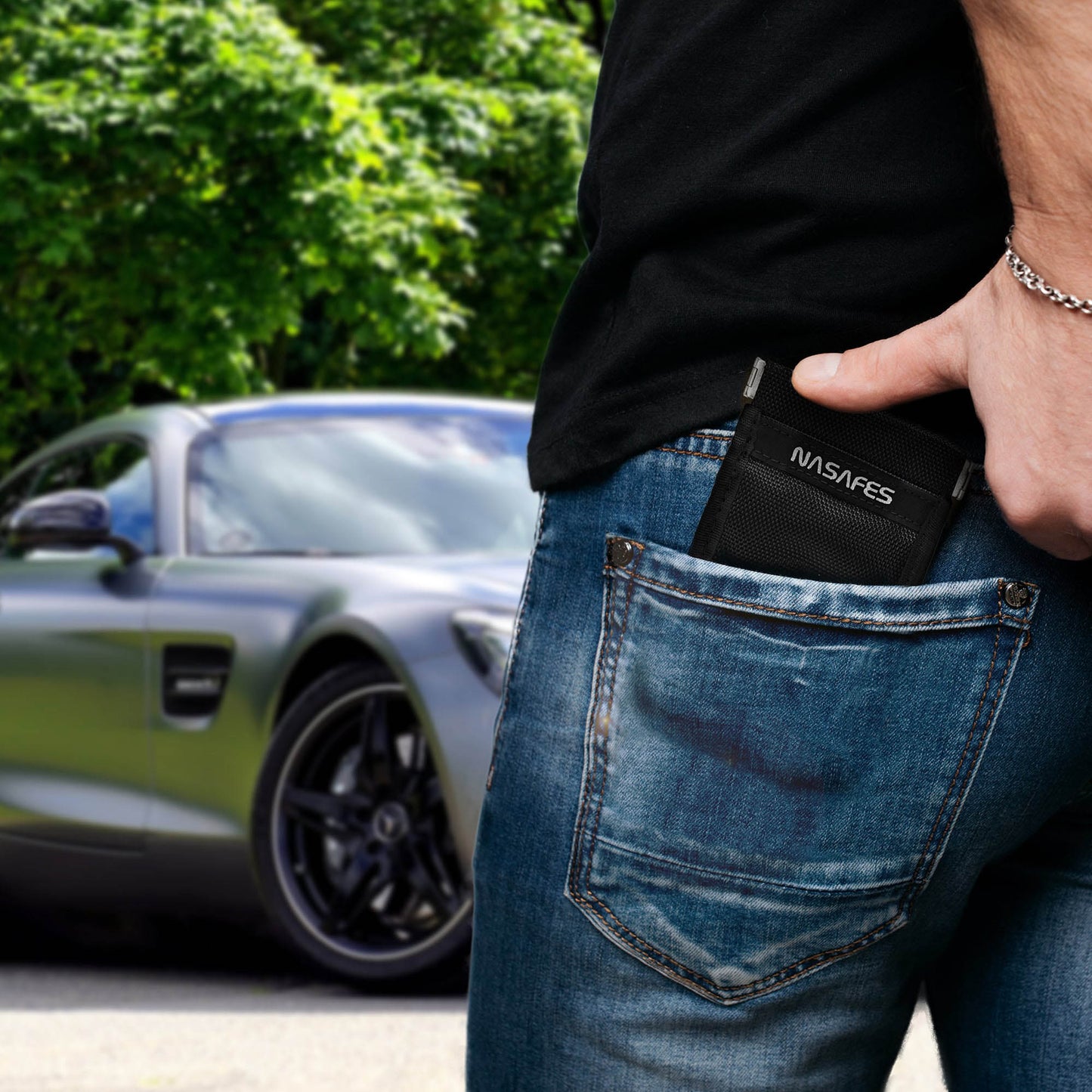Ein Mann steckt die Schlüsseltasche Keyless Go Schutz in seine Hosentasche. Er steht vor einem grauen Sportwagen, der wahrscheinlich ihm gehört. Mit dem Faraday Bag möchte er Signaldiebstahl seines Funkschlüssels verhindern.